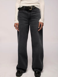 Person wearing belted black jeans and a white long-sleeve shirt on a plain background