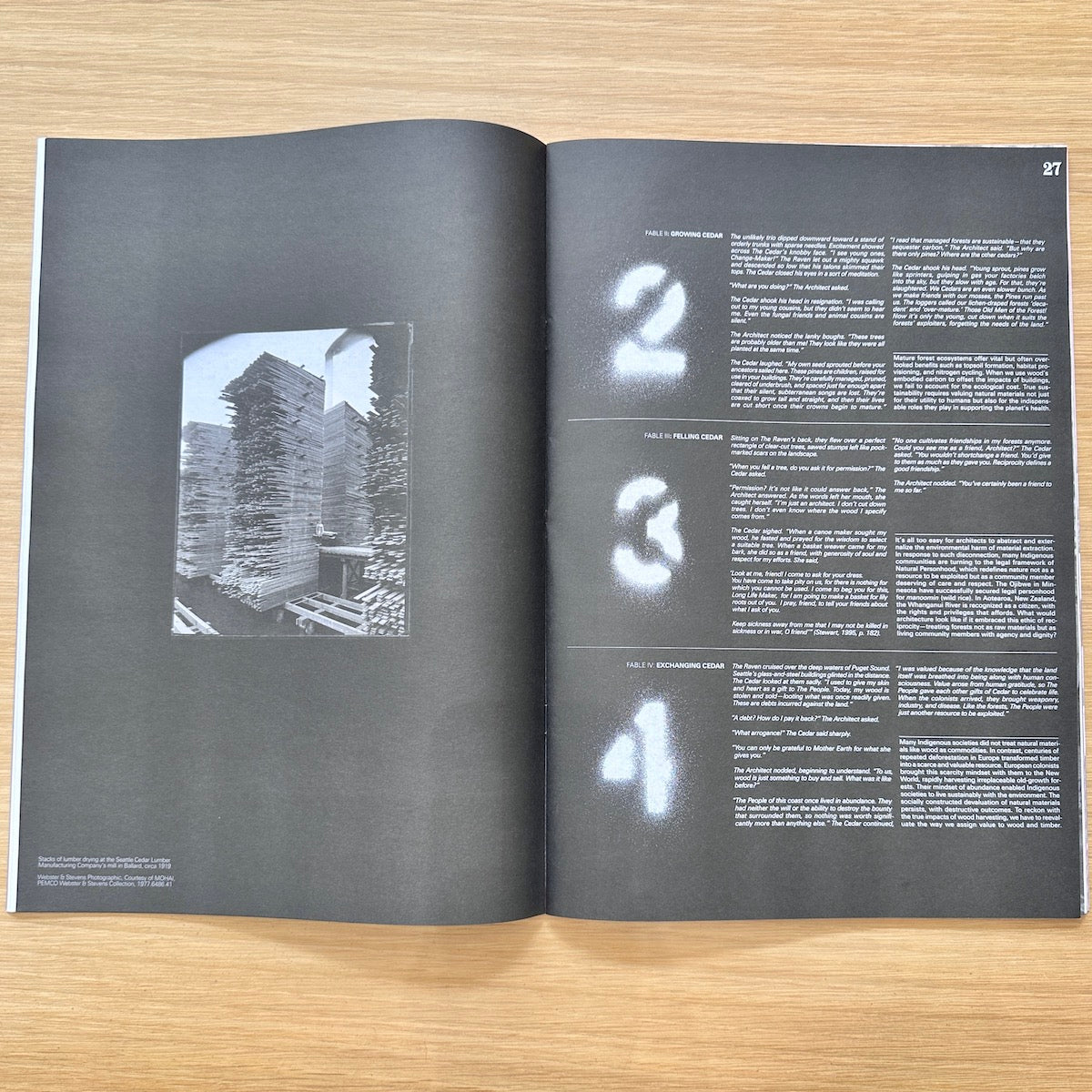 An open book or magazine spread laid flat on a light wood surface, showing a black-and-white architectural photograph on the left page and a two-column text layout with large white numbers 2, 3, and 4 on the right page.