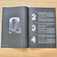 An open book or magazine spread laid flat on a light wood surface, showing a black-and-white architectural photograph on the left page and a two-column text layout with large white numbers 2, 3, and 4 on the right page.