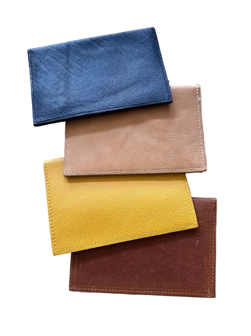 Four leather passport holders in black, tan, mustard yellow, and caramel-brown, stacked on a white background.