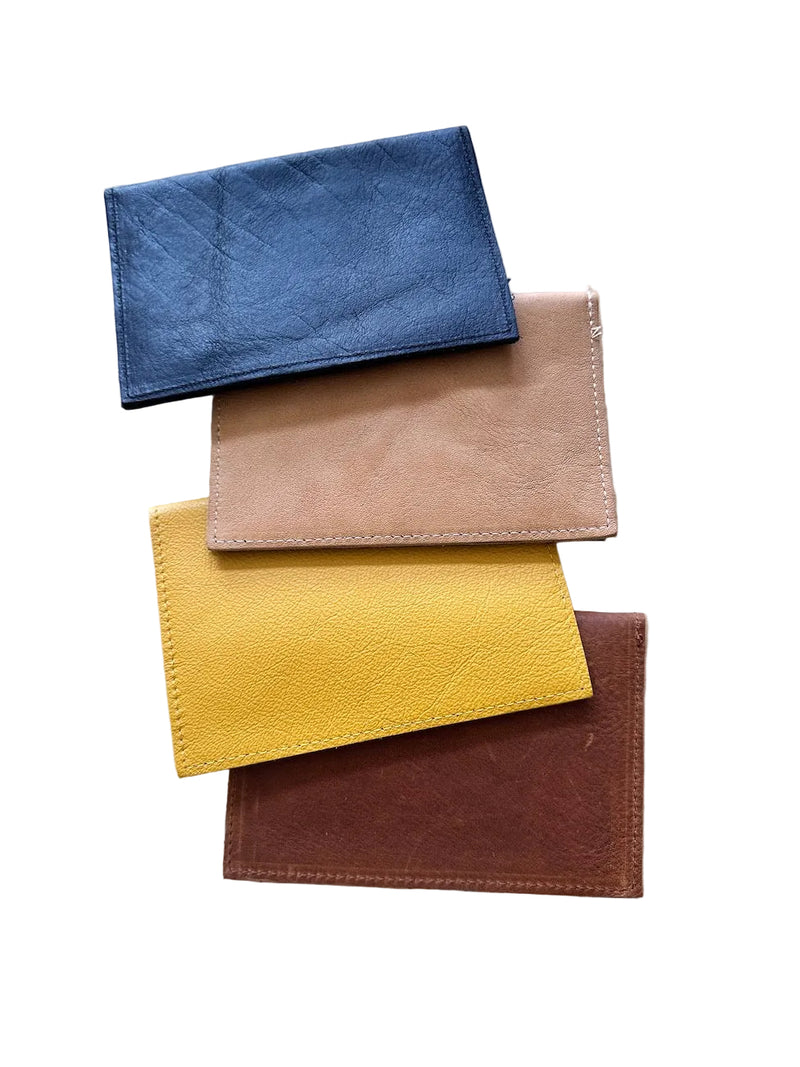 Four leather passport holders in black, tan, mustard yellow, and caramel-brown, stacked on a white background.