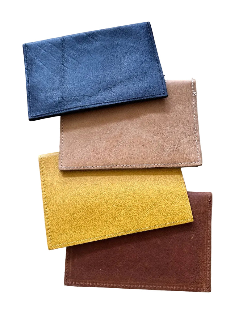 Four leather passport holders in black, tan, mustard yellow, and caramel-brown, stacked diagonally on a white background.