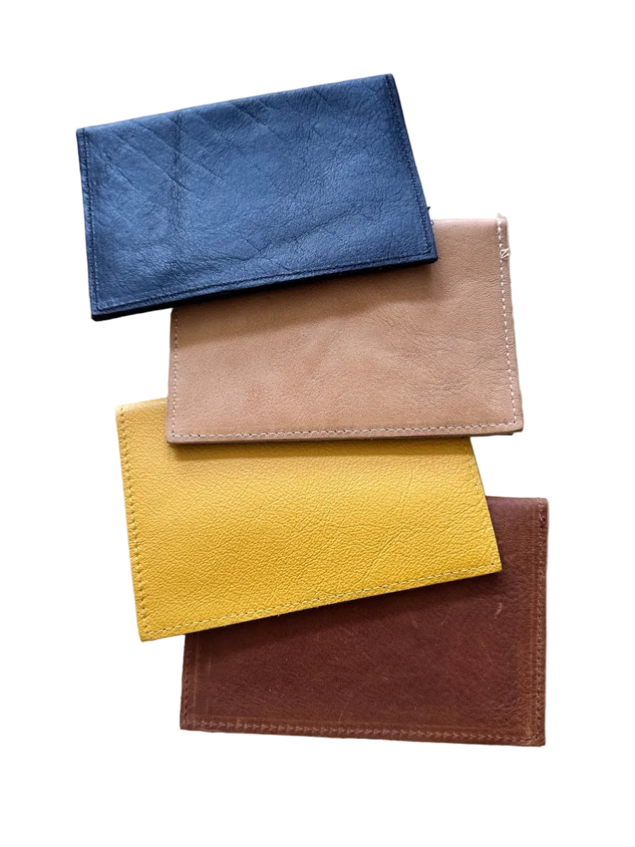 Four leather passport holders in black, tan, mustard yellow, and caramel-brown, stacked on a white background.