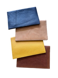 Four leather passport holders in black, tan, mustard yellow, and caramel-brown, stacked on a white background.
