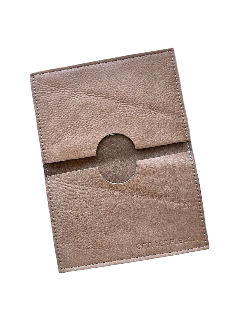 A tan leather card holder with a circular cutout and debossed 'erm templeton' branding, laid flat on a white surface.
