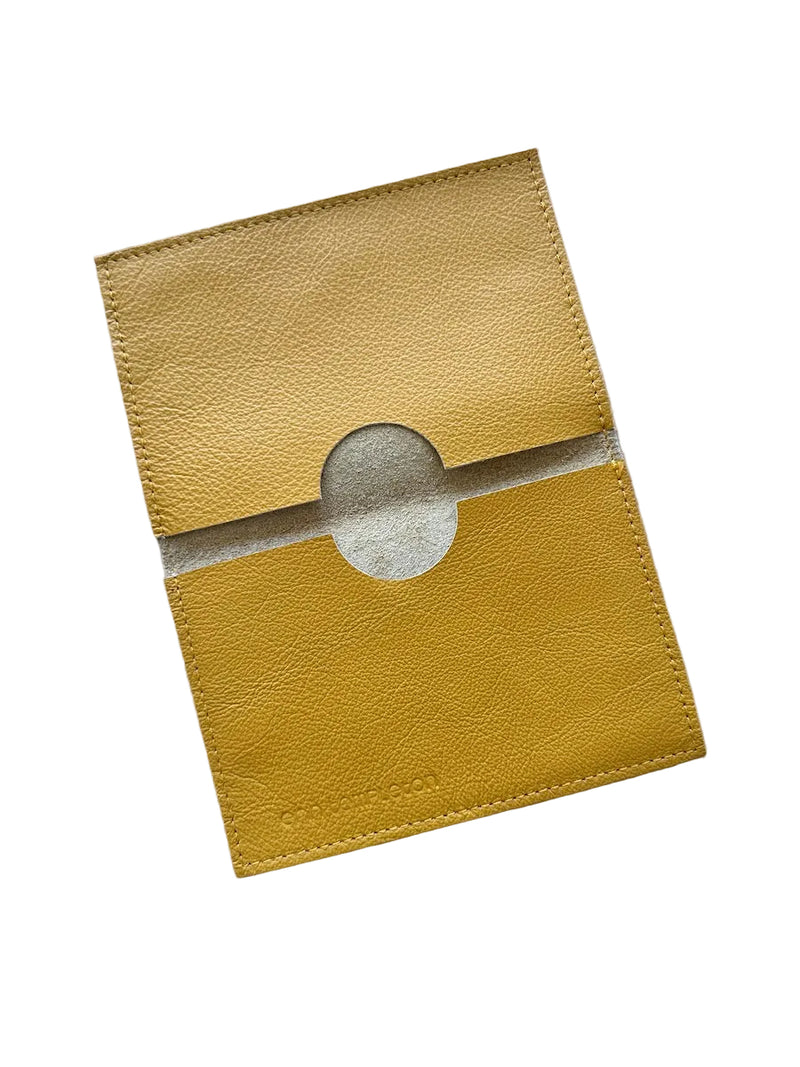 A mustard yellow textured leather passport holder with a circular cutout in the center, displayed on a white surface.