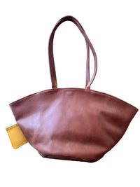 A brown leather tote bag with a wide, curved top and two shoulder straps, with a small yellow wallet is partially tucked into a side pocket of the bag.