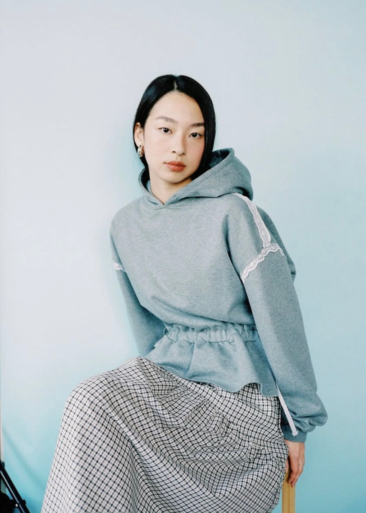 Woman wearing a gray hoodie and plaid skirt on a light blue background
