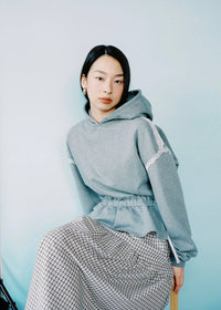Woman wearing a gray hoodie and plaid skirt on a light blue background
