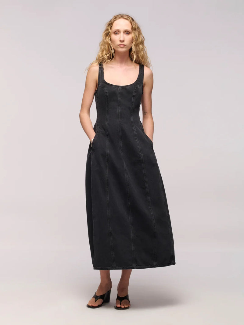 Woman wearing a black denim midi dress with black thong heels on a light grey background