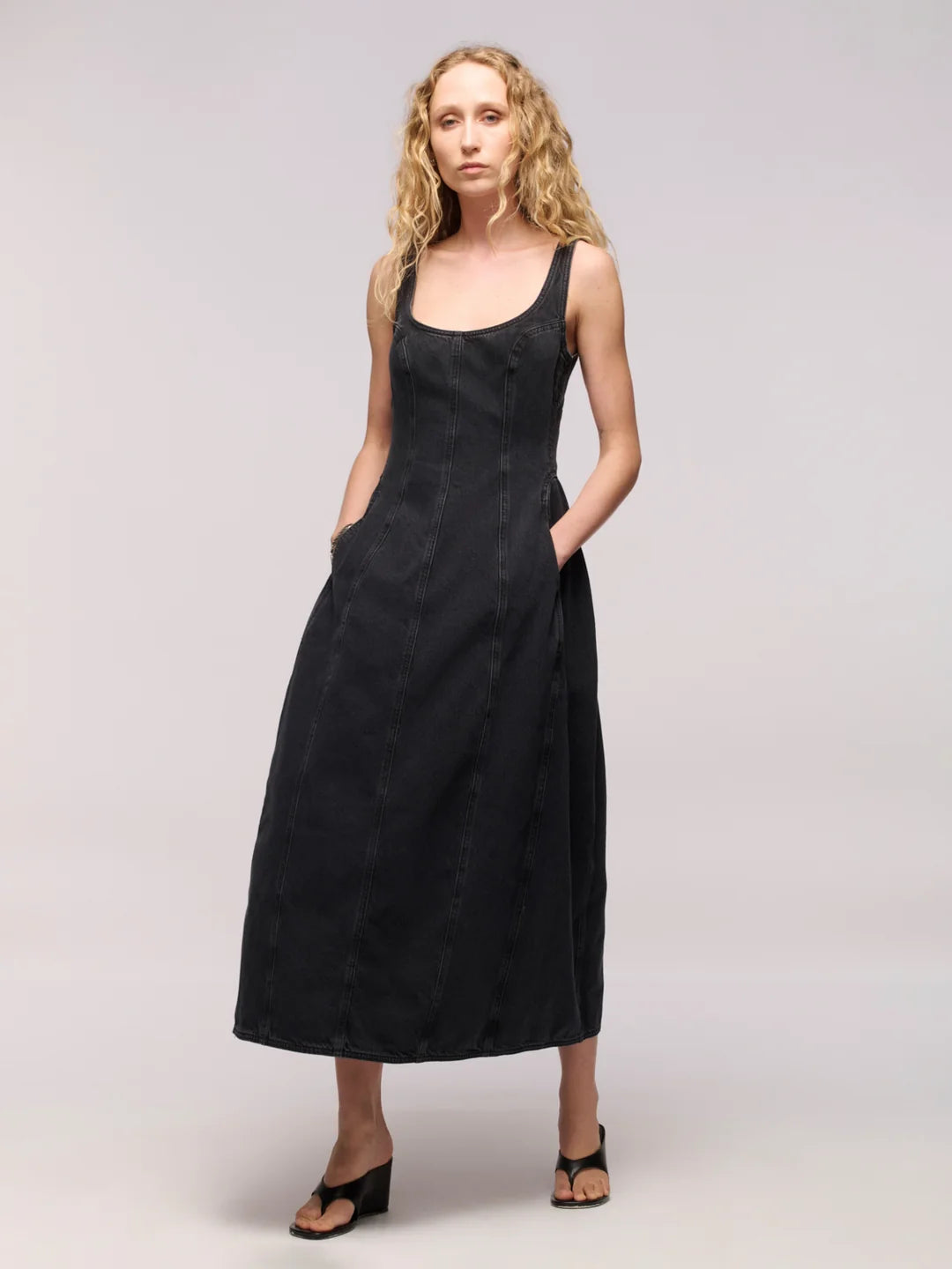 Woman wearing a black denim midi dress with black thong heels on a light grey background