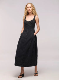 Woman wearing a black denim midi dress with black thong heels on a light grey background