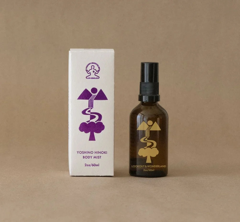 Amber bottle with a gold graphic design print and text LOOKOUT & WONDERLAND next to a white box of packaging with purple design print and text YOSHINO HINOKI BODY MIST on a Kraft paper background
