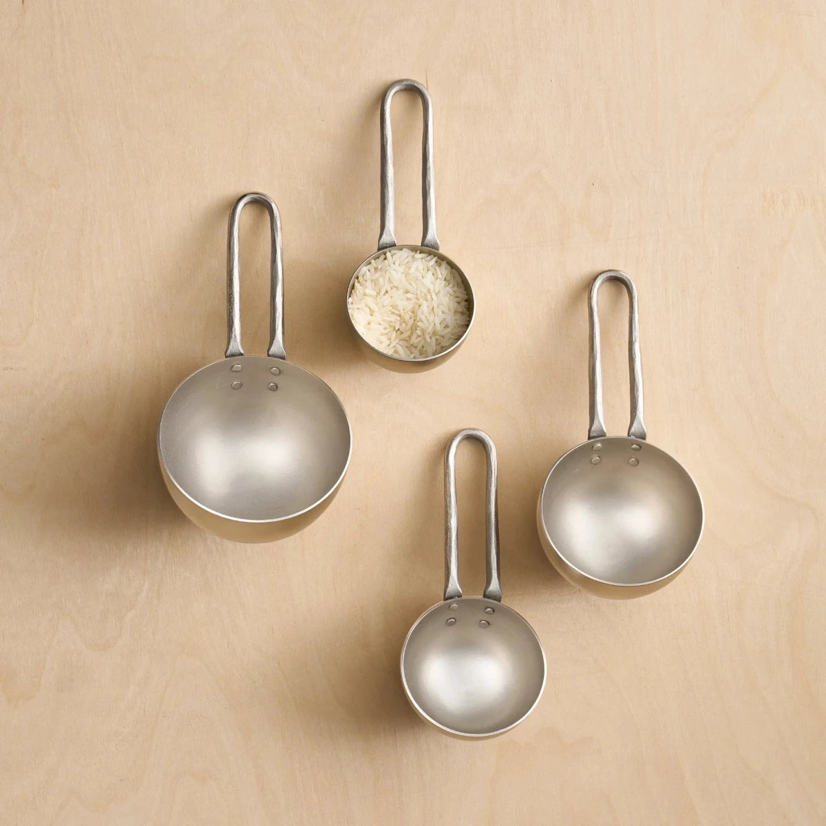 Four round pewter measuring scoops on a wooden surface