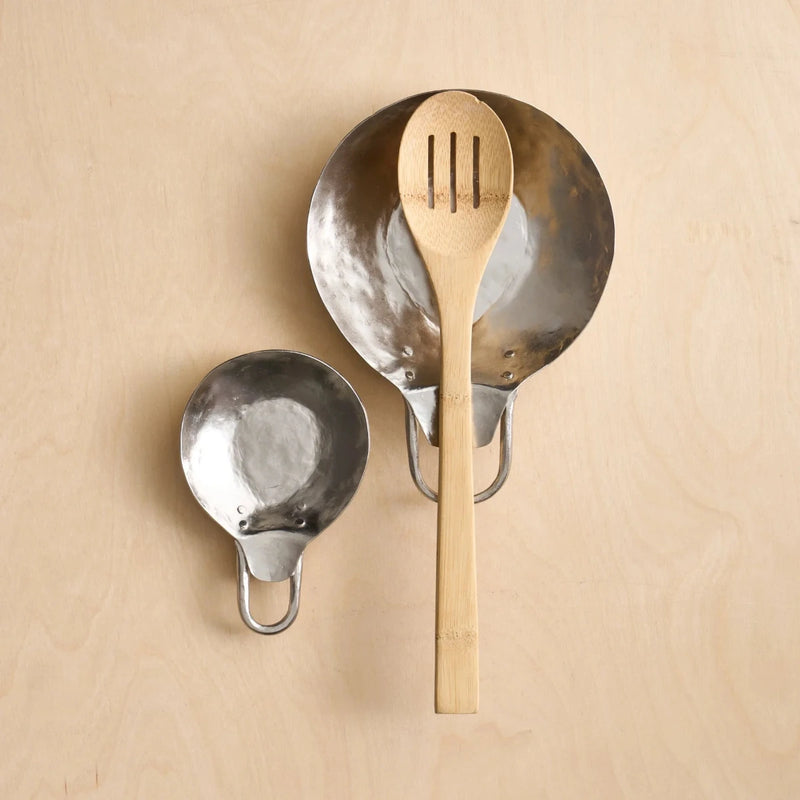 Set of two pewter spoon rests with wooden spoon on a wooden surface