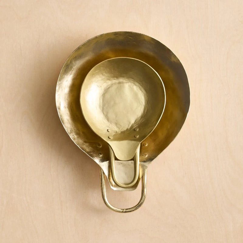 Pair of brass spoon rests stacked on a wooden surface