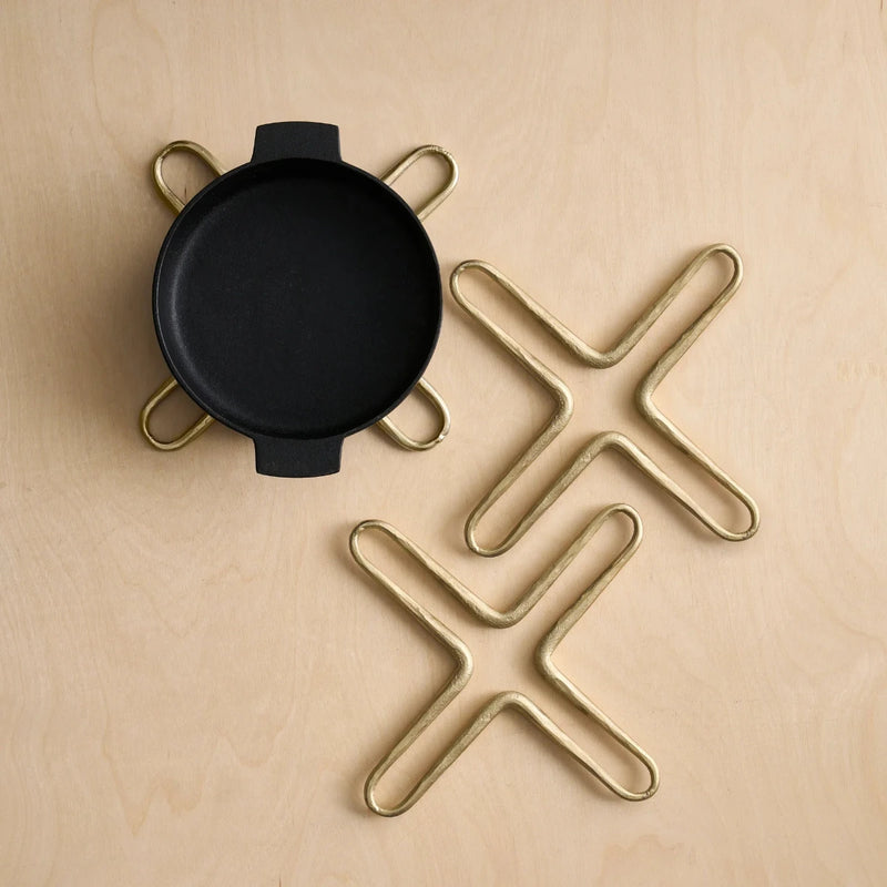 X shaped brass trivets and a black pot on a wooden surface