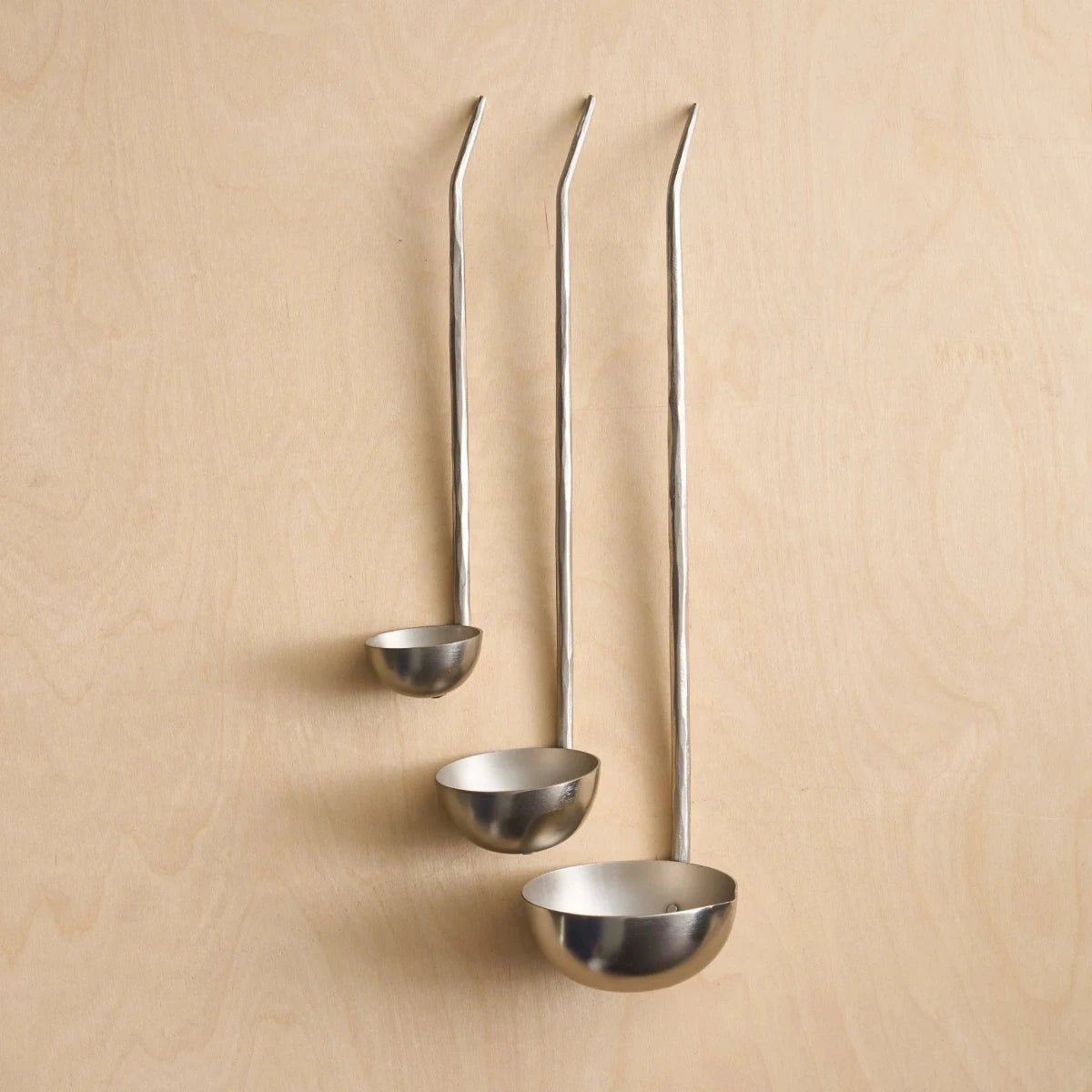 Set of three silver ladles on a wooden surface