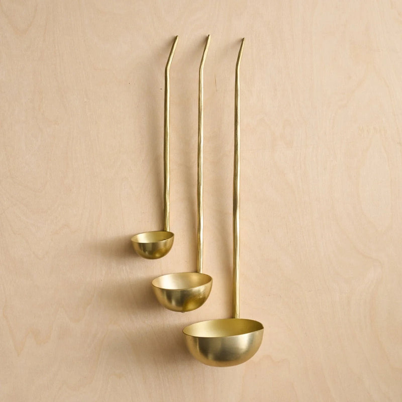 Set of three brass ladles on a wooden surface