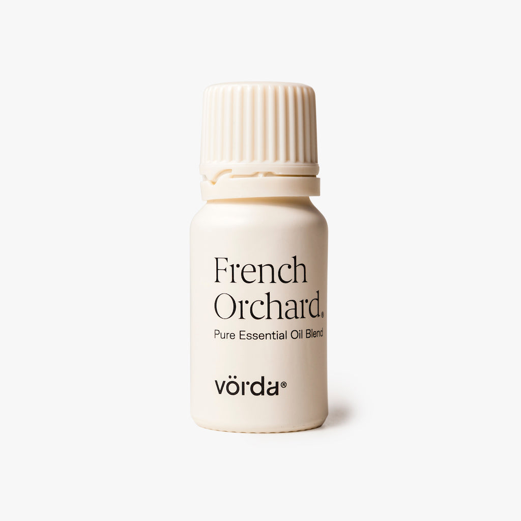 A small cream-colored bottle of vörda French Orchard Pure Essential Oil Blend with a ribbed screw cap, set against a clean, light gray background.