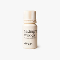 Off-white bottle with a ribbed cap labeled 'Midnight Woods Pure Essential Oil Blend and 'vörda' on a light grey background