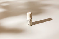 A small white bottle labeled 'Midnight Woods' by the brand 'vörda', placed on a warm off-white surface with soft shadows cast across it.