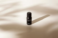 A small black bottle of Vorda Eucalyptus Pure Essential Oil with a black cap, standing on a warm beige surface with soft shadows cast across it.