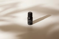A small black bottle of Spike Lavender essential oil by Vorda, standing on a warm beige surface with soft leaf shadows cast across it.