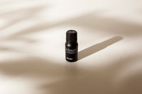 A small black bottle of Hinoki Essential Oil, standing upright on a beige surface with soft shadows cast across it.