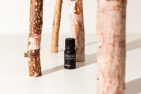 A small black bottle labeled Hinoki with white text stands on a white surface between several tree trunks used as decorative props.