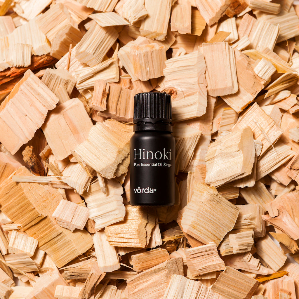 A small black bottle of Vörda Hinoki pure essential oil droplets placed on top of a bed of light wood shavings.