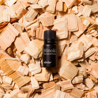 A small black bottle of Vörda Hinoki pure essential oil droplets placed on top of a bed of light wood shavings.