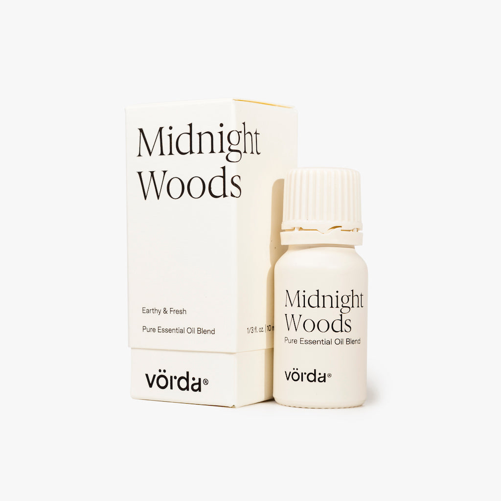 A small white bottle of Vörda Midnight Woods pure essential oil blend stands in front of its matching white box on a clean white background.