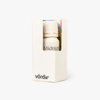 A small white bottle with a ribbed cap displayed inside a tall white box with a front window. The box is printed with the brand name 'vörda' near the bottom and shows the scent name 'Midnight' through the window.