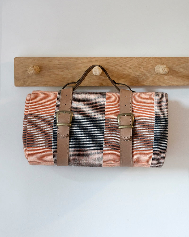 Rolled picnic blanket with leather straps hanging on a wooden rack 