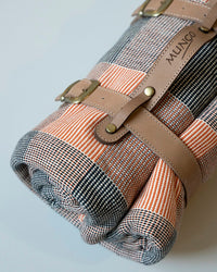 Rolled picnic blanket with plaid pattern and brown leather straps 