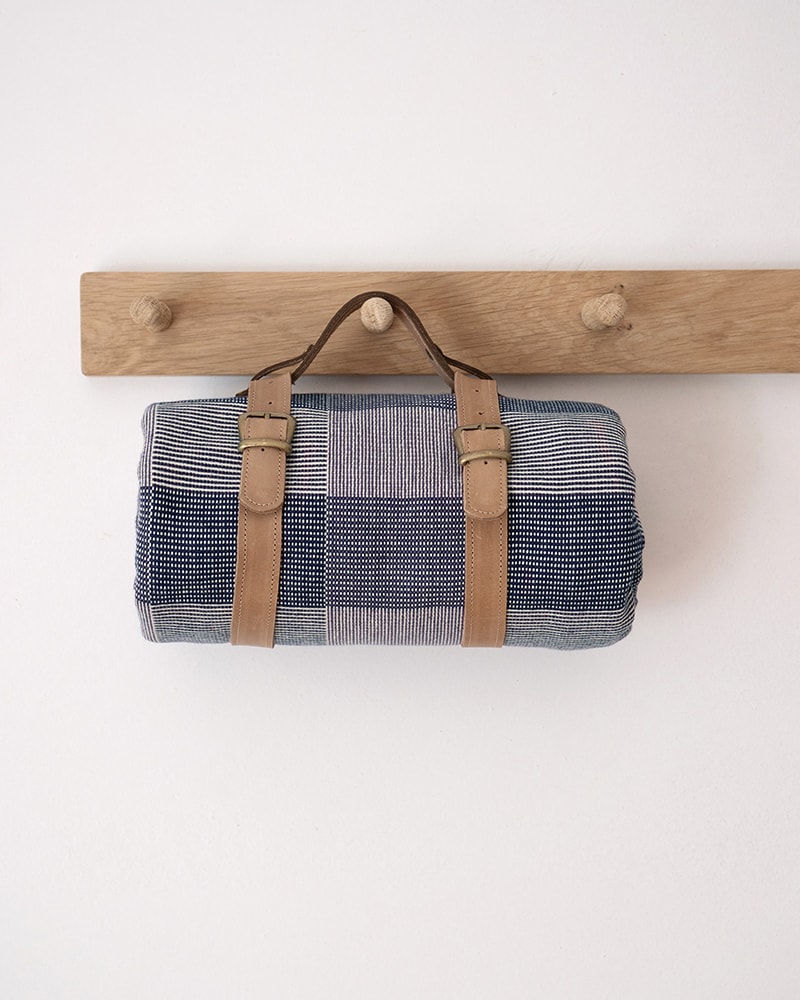 Plaid rolled picnic blanket with brown leather straps hanging on a wooden rack 