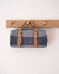Plaid rolled picnic blanket with brown leather straps hanging on a wooden rack 
