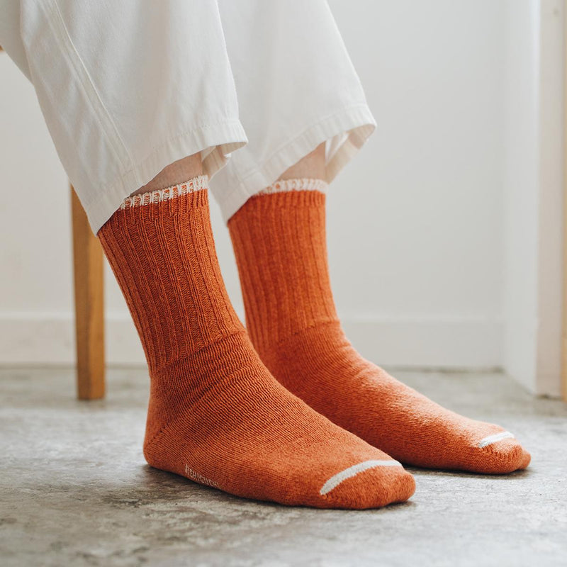 feet of person sitting down wearing orange socks and white pants on neutral background
