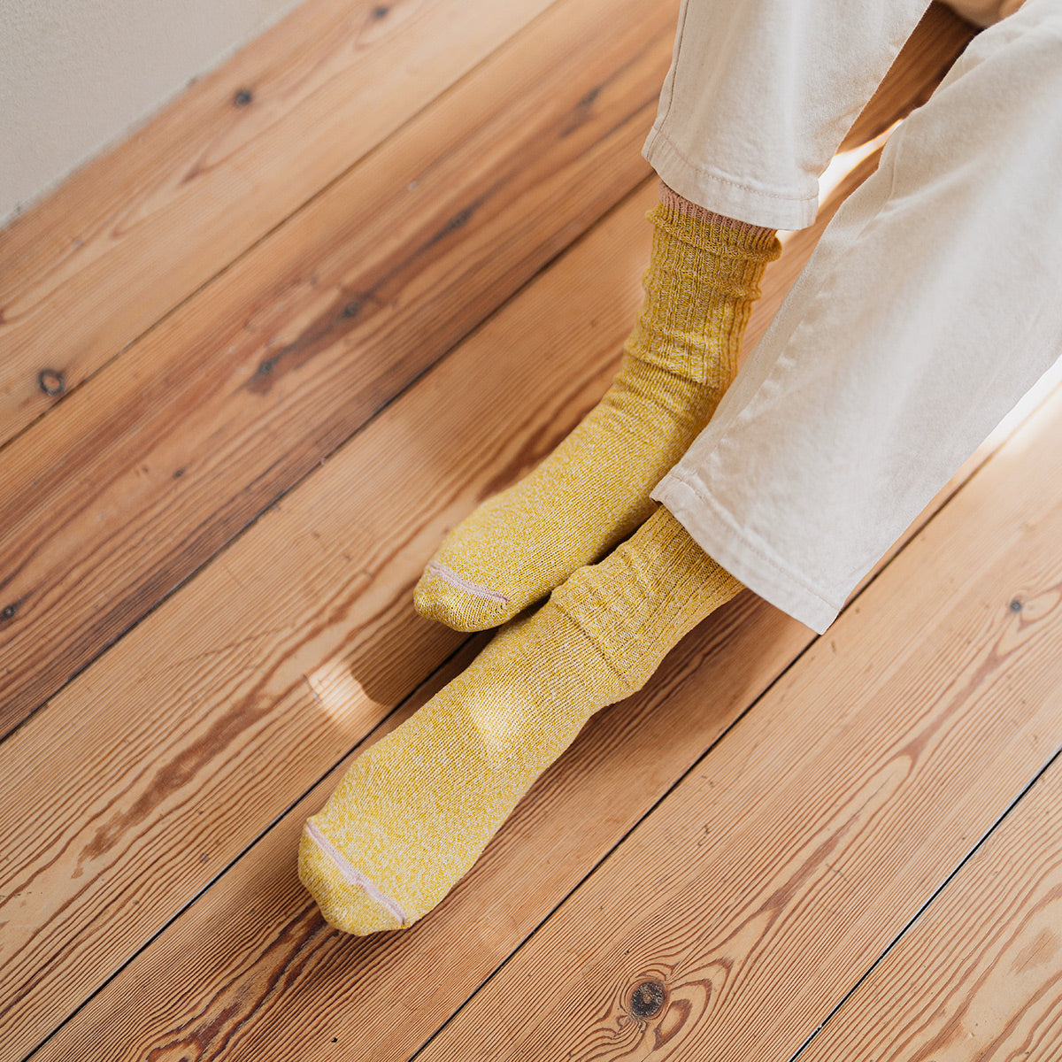 Person wearing yellow socks and white pants on a wooden floor