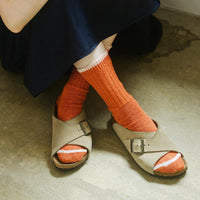 feet of person sitting on the ground with legs crossed wearing orange socks and sandals