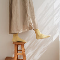 Person standing on a wooden stool wearing yellow socks and a beige skirt