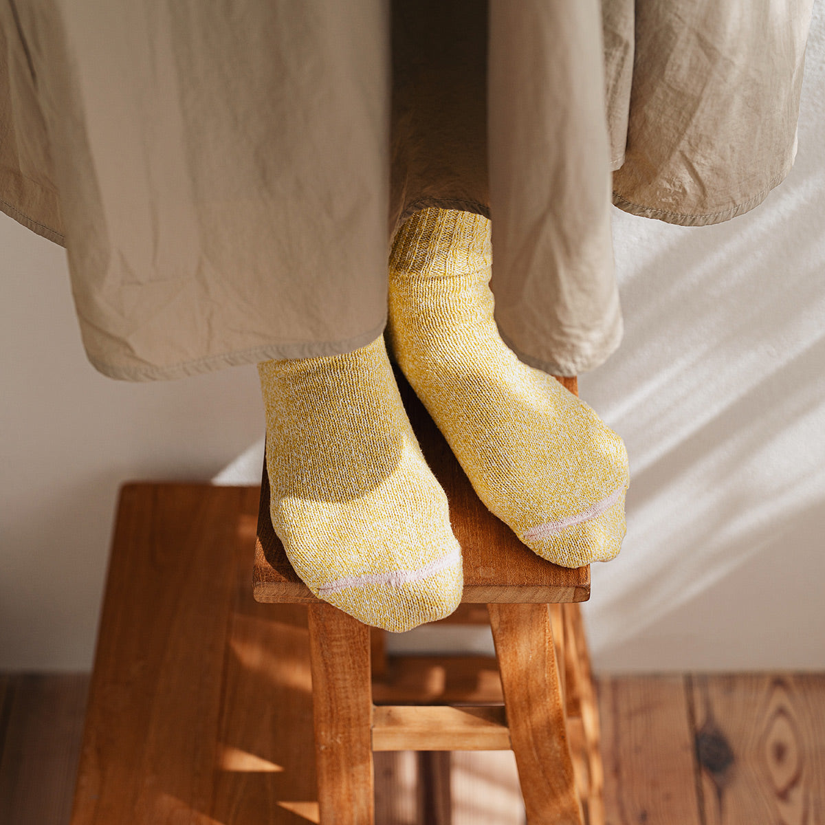 feet on a wooden stool with yellow socks and a beige skirt