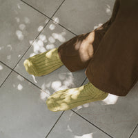 overview of person's legs wearing chartreuse socks and brown pants on a tiled surface in filtered light