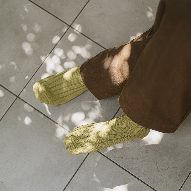 overview of person's legs wearing chartreuse socks and brown pants on a tiled surface in filtered light