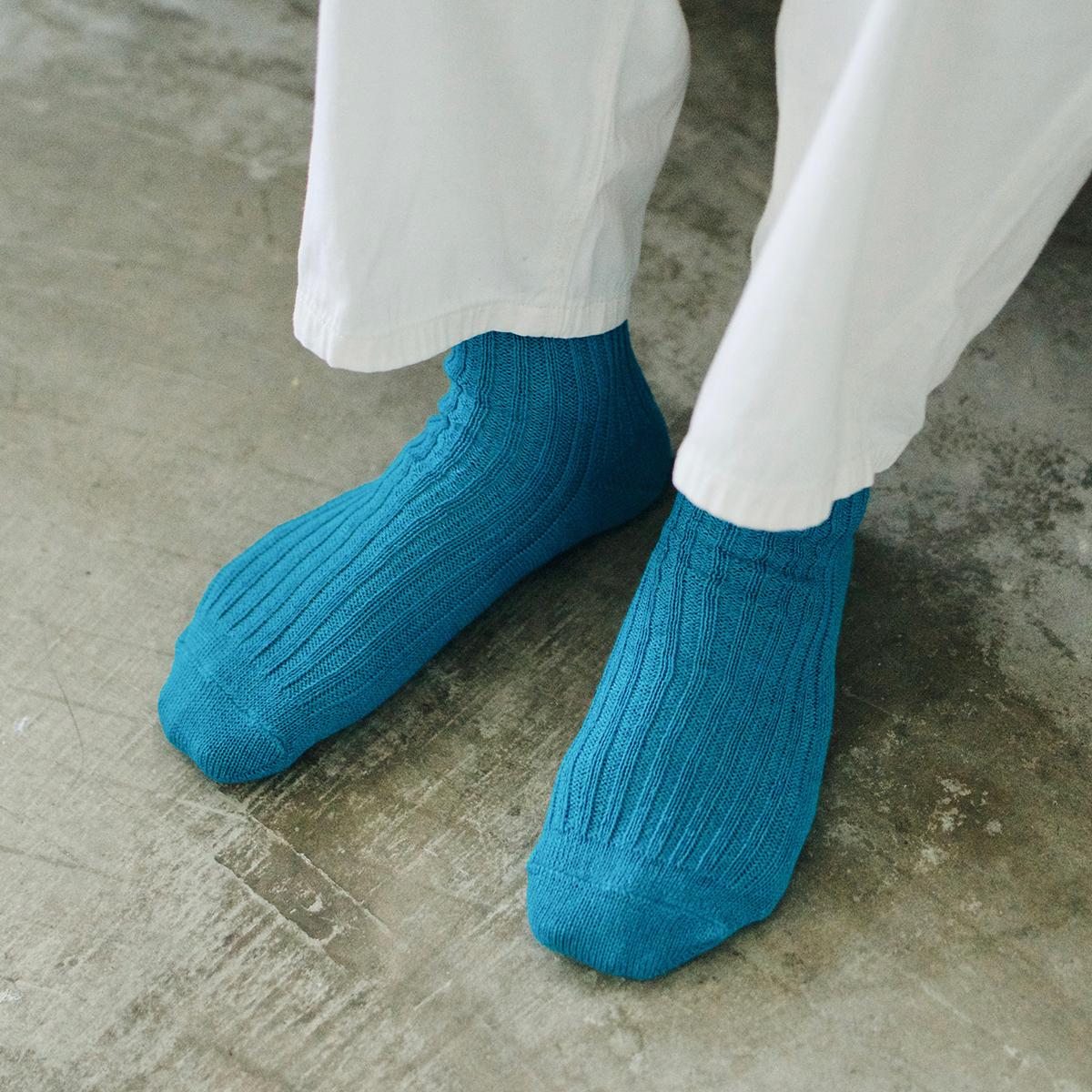 feet of person wearing teal socks and white pants on concrete floor