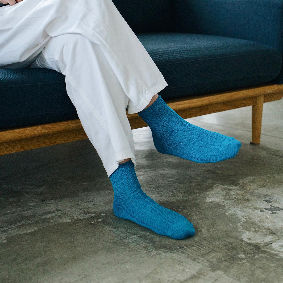 legs of person wearing teal socks and white pants sitting on couch