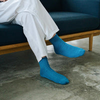 legs of person wearing teal socks and white pants sitting on couch