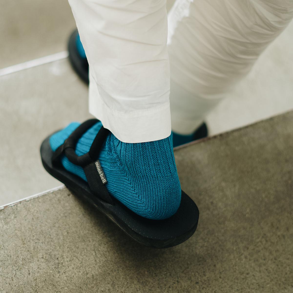 back of feet of person going down stairs wearing teal socks, black sandals, and white pants