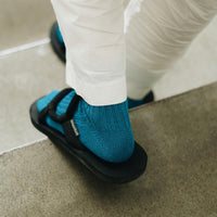 back of feet of person going down stairs wearing teal socks, black sandals, and white pants